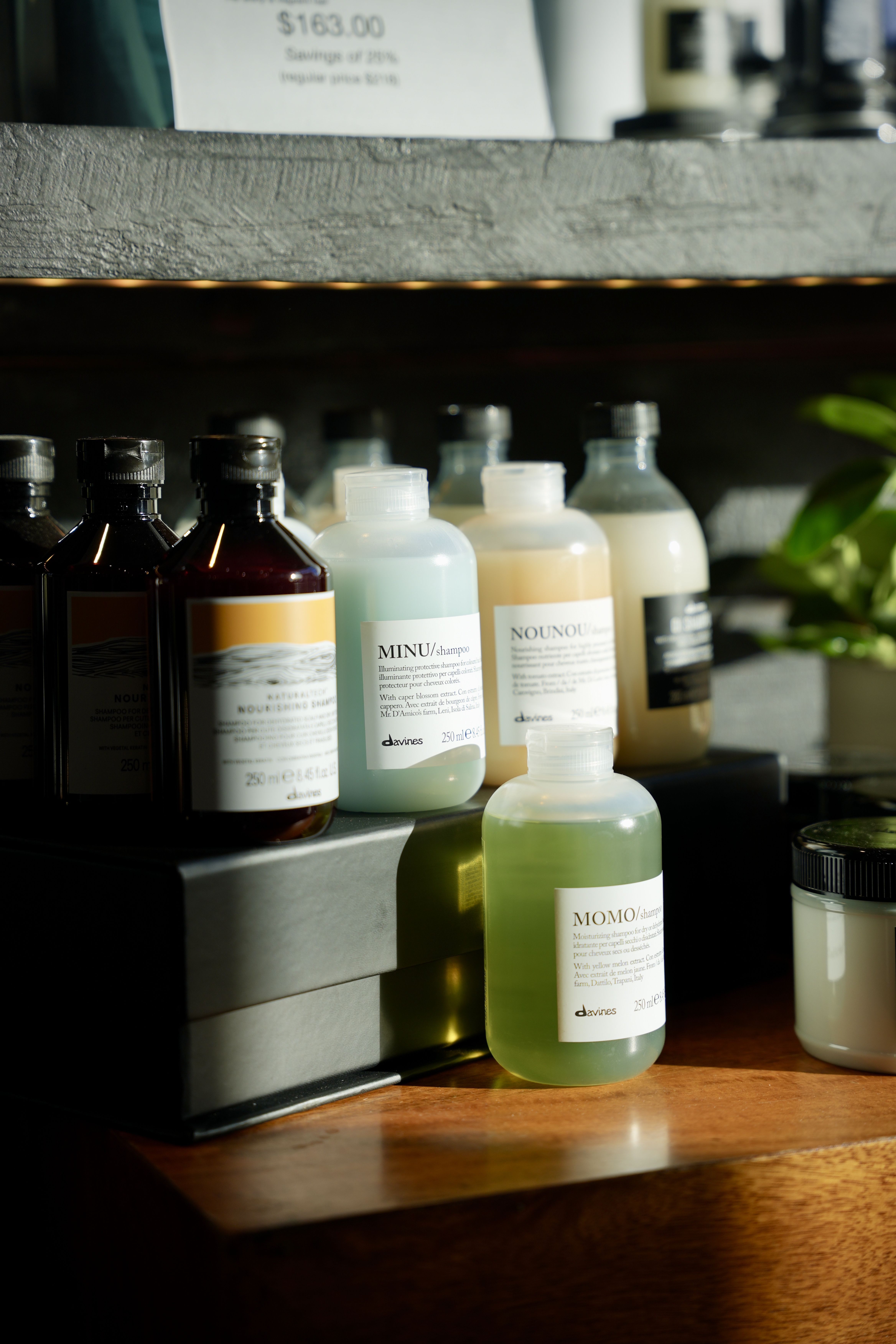 A row of Davines bottles — Minu, Nounou, Momo — on a dark shelf in warm light
